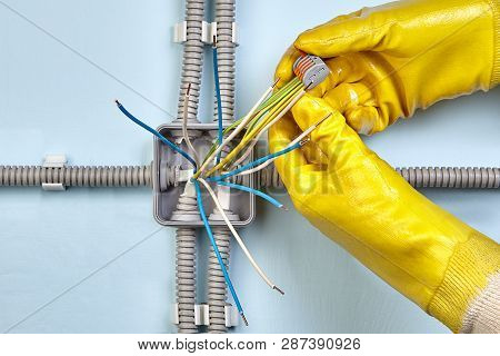 Electrician In Protective Yellow Gloves Uses Spring Terminals To Bind Wires Together Durind Mounting