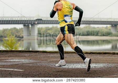 Male Runner In Compression Socks And Protective Arm Sleeves Run River Embankment