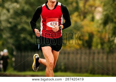Male Athlete Running Marathon In City Background Of Green Trees