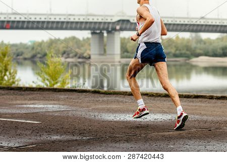 European Man Runner Running In Embankment Of River Next To Bridge