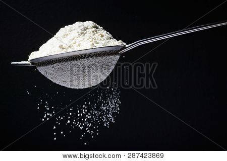 Flour Is Poured Into A Sieve, Which Sifts It. Dark And Black Background. Flour Movement.