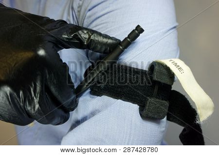 Person In Black Medical Gloves Applies The Tourniquet To His Hand To Prevent Bleeding During The Fir