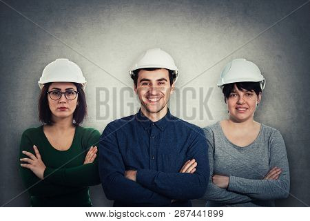 Team Of Three Confident, Positive Thinking Engineers Wearing Protective Helmet And Holding Arms Cros