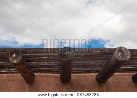 Exterior Red Adobe Building With Beams And Wood Sun Screen Slats, Blue Sky And Clouds, Horizontal As