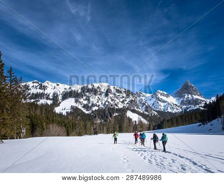 Group Of Adults Snowshoeing On Snowy Plateau Kaiserau With Mountain Admonter Kalbling On A Sunny Win