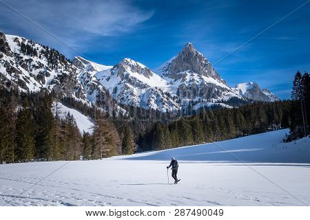 Man Snowshoeing On Snowy Plateau Kaiserau With Mountain Admonter Kalbling On A Sunny Winterday In St
