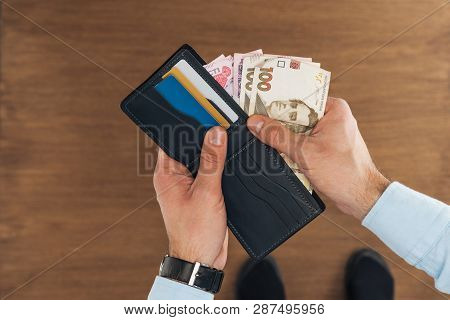 Top View Of Man Taking From Wallet With Credit Cards Hryvnyas Banknotes On Wooden Background