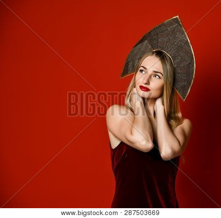 Beautiful Sexy Blonde Russian Girl In Traditional Kokoshnik Hat, Velvet Festive Dress On A Red Backg