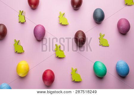 Colorful Easter eggs and wooden Easter Bunnies as attribute of Easter celebration. Pink background.