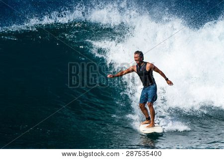 MAUI / USA - 14 DECEMBER 2018: Hawaiian adult surfer rides the ocean wave with smile and happy face. Honolua surf spot on the north of Maui