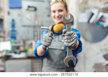 Woman mechanic showing tools to the camera holding wrench in her hand