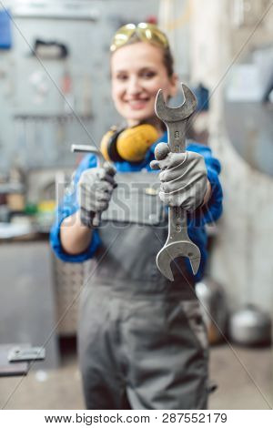 Woman mechanic showing tools to the camera holding wrench in her hand