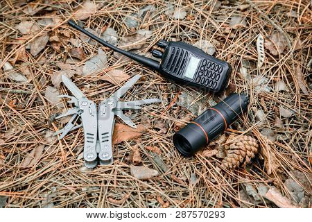 Monocle, Radio Set And Multitool Knife On The Ground Covered With Pine Needles