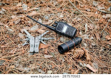 Monocle, Radio Set And Multitool Knife On The Ground Covered With Pine Needles
