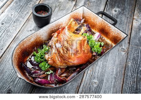 Traditional Bavarian schweinshaxe with onion as closeup in a rustic stewpot on an old wooden board 