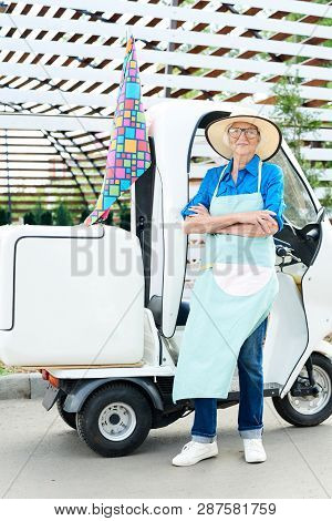 Full Length Portrait Of Senior Woman Posing In Garden Standing Next To Moving Cart With Arms Crossed