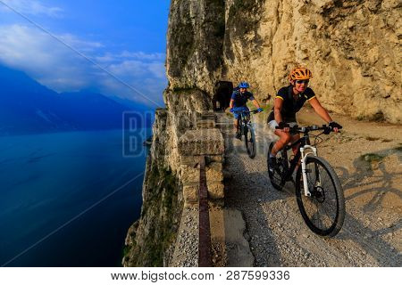 Cycling woman and man riding on bikes at sunrise mountains and Garda lake landscape. Couple cycling MTB enduro flow sentiero ponale trail track. Outdoor sport activity.