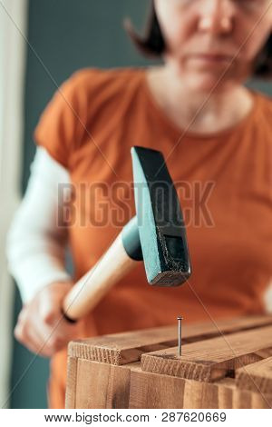 Female Carpenter Hammering Nail Into Wooden Crate In Small Business Woodwork Workshop, Selective Foc