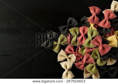 Farfalle Raw Farfallini Colored Italian Pasta On A Wood Black Textured Background. Close-up View Fro