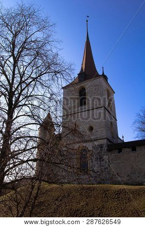Stone Tower Of The 7th Century In Swiss Village Church. Church Tower Attached To Defense Wall Of The