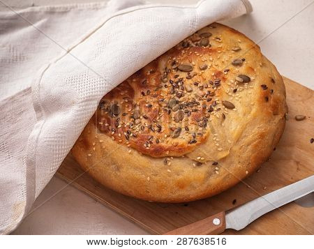 Freshly Baked Homemade Bread With Seeds And Sesame Of A Round Shape Under A Light Linen Napkin On A 