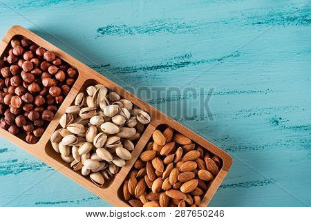 Compartmental Dish With Nuts On Blue Wooden Table. Hazelnut, Almond, Pistachio.