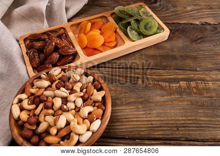 Dates, Dried Apricots And Kiwis In A Compartmental Dish And Assortment Of Nuts In Wooden Bowl On A D