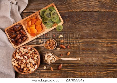 Dates, Dried Apricots And Kiwis In A Compartmental Dish And Assortment Of Nuts In Wooden Bowl On A D