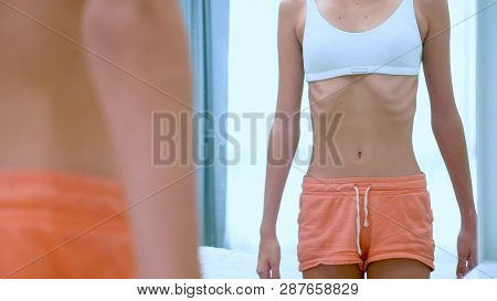 Anorexia Concept - Slim Teen Girl, With Protruding Ribs Looking At Her Reflection In The Mirror