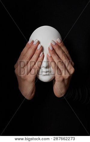 Woman's fingers close eyes of gypsum mask face on a black background. See no evil. Concept three wise monkeys. Place for text.