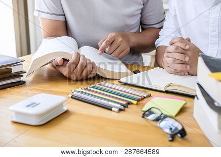 High School Tutor Or College Student Group Sitting At Desk In Library Studying And Reading, Doing Ho