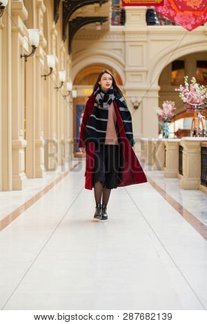 Full body portrait. Young beautiful woman in stylish in a long burgundy coat, indoor shop
