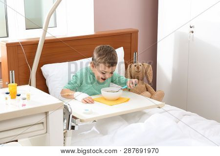 Little Child With Intravenous Drip Eating Soup In Hospital Bed