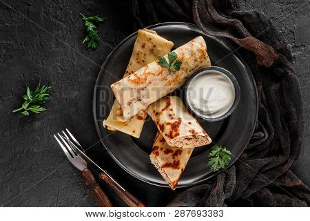 Crepes With Chopped Meat, Greens And Sour Cream On Black Plate Over Dark Background. Pancake Week Or