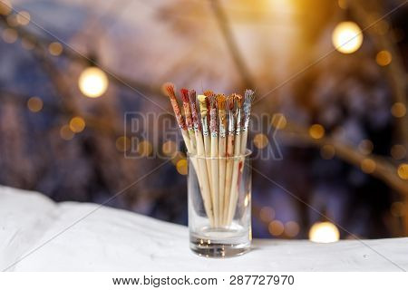 Paint Brushes In A Glass Jar With Remnants Of Paint.
