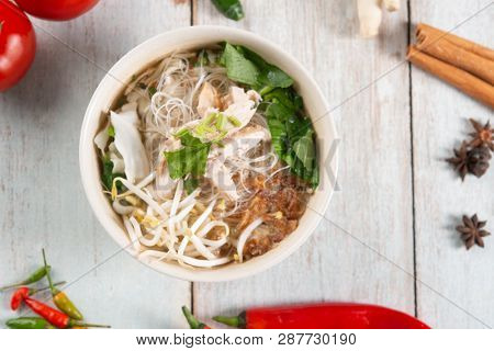 Asian rice noodles soup with vegetables and chicken in bowl. Top view flat lay on wooden background.