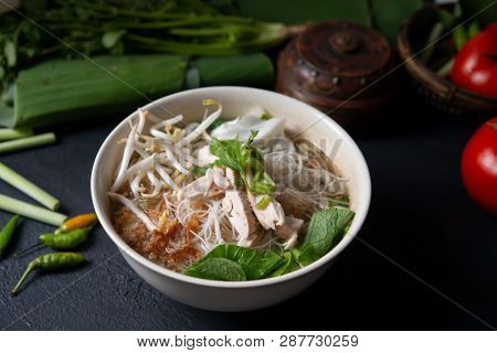 Asian rice noodles soup and chicken in bowl on dark background.