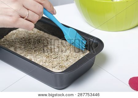 Baking Bread At Home. Wholemeal Dough Lies In Bread Pan. A Woman Distributes Sunflower Seeds Over Th