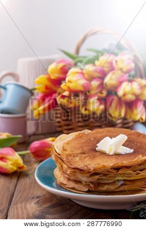 Lots Of Thin Pancakes On A Wooden Background Or Table, And A Basket With Fresh Red-yellow Tulips. Ba