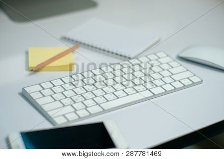 Selective Focus On White Keyborad On The Desk With Defocused Stationary, Mouse, And Mobile Phone In