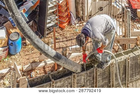 Limassol, Cyprus - April 3, 2018:  Man Standing On Shuttered Wall Bending Over And Pouring Cement In