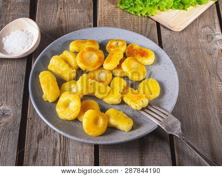 Fried Potato Gnocchi On A Gray Ceramic Plate, Leaves Of Fresh Leaf Lettuce Lie On An Unpainted Kitch