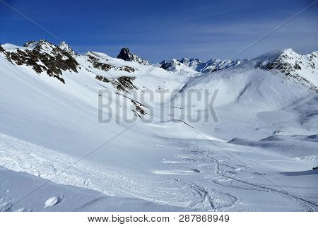 Snowy Ski Slope With Print From Skis, Snowboards And Foot, Snow Mountains And Blue Sky With Clouds