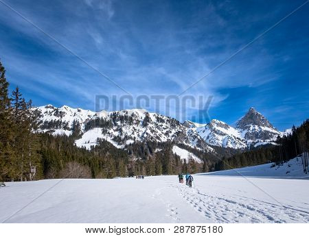 Group Of Adults Snowshoeing On Snowy Plateau Kaiserau With Mountain Admonter Kalbling On A Sunny Win