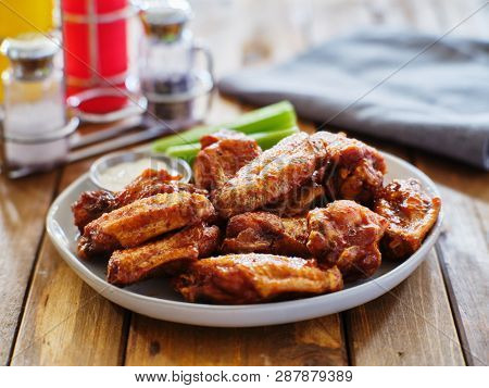 plate of bbq chicken wings with ranch dip and celery sticks on wooden table
