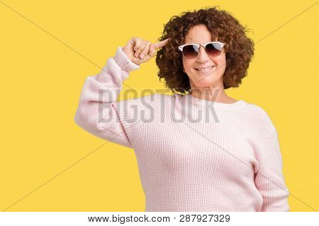 Beautiful middle ager senior woman wearing pink sweater and sunglasses over isolated background Smiling pointing to head with one finger, great idea or thought, good memory