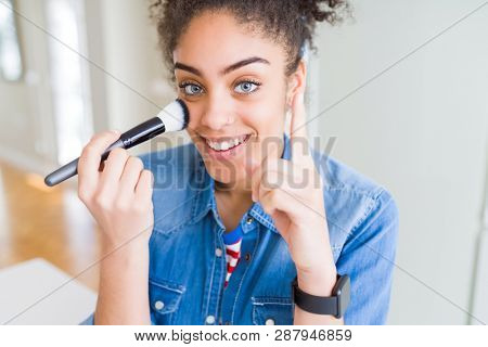Young african american girl appying blush using make up brush surprised with an idea or question pointing finger with happy face, number one
