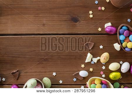 easter, sweets and confectionery concept - chocolate eggs and candy drops on wooden background