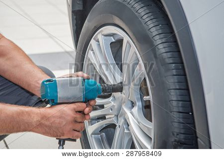 Car Repair: Wheel Replacement Closeup. Mechanic Screwing Or Unscrewing Car Wheel At Car Service Gara