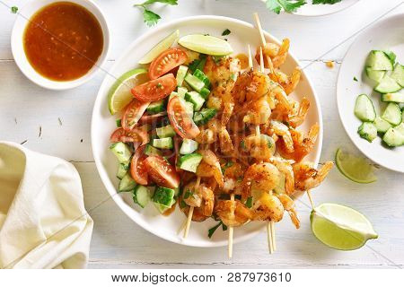 Tasty Prawns Skewers With Greens, Spices, Lime And Sauce On White Plate Over Wooden Table. Grilled S